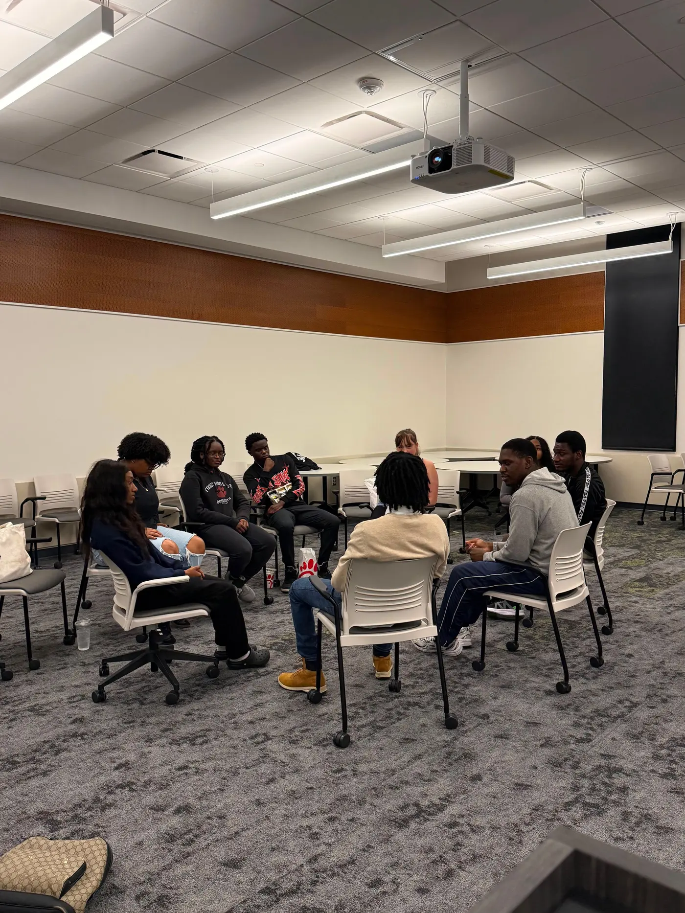 A ring of chairs in a meeting room with students seated around it, turned towards each other.