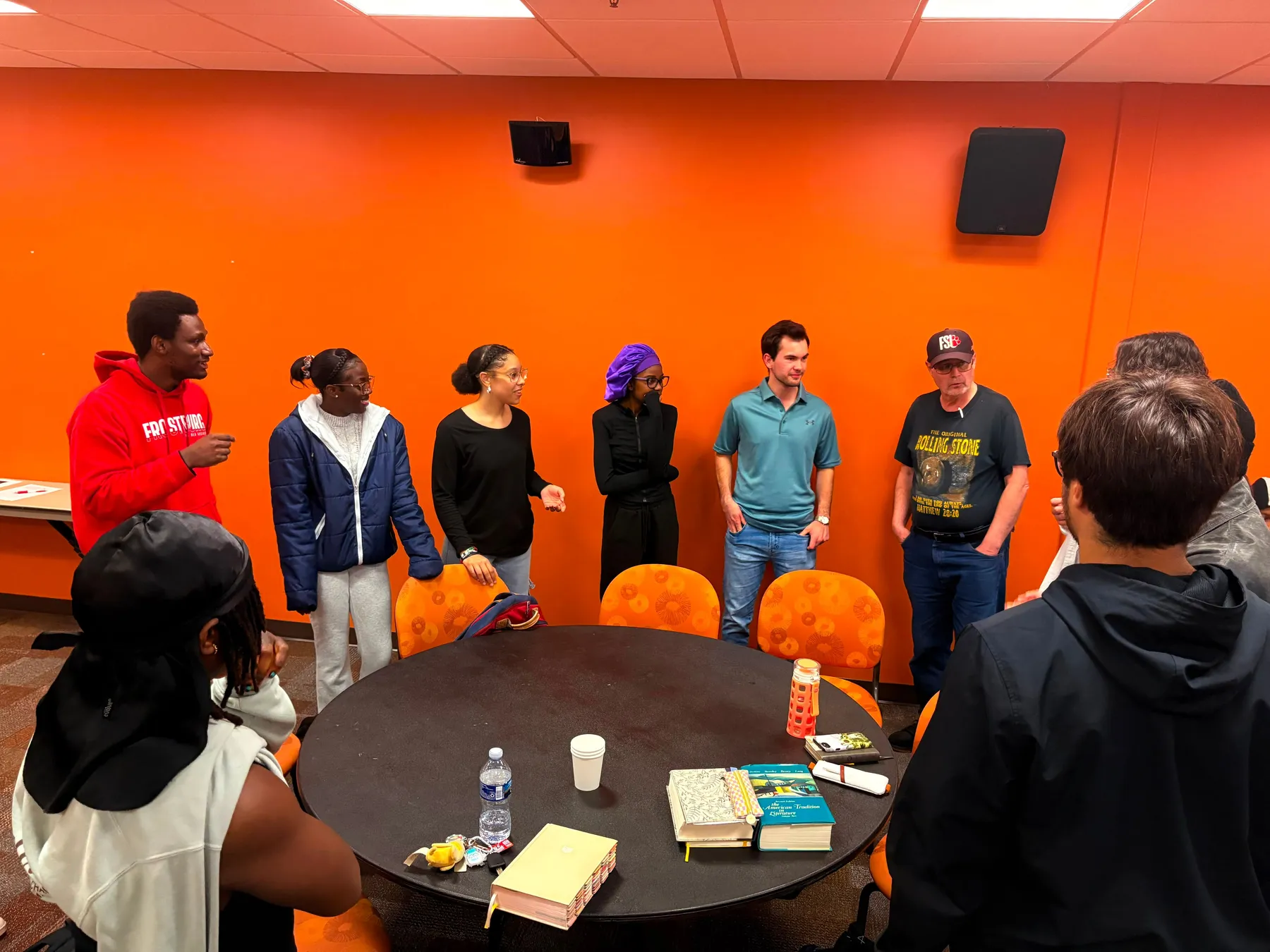 Students standing in a semicircle around a table laid with open Bibles and study books.