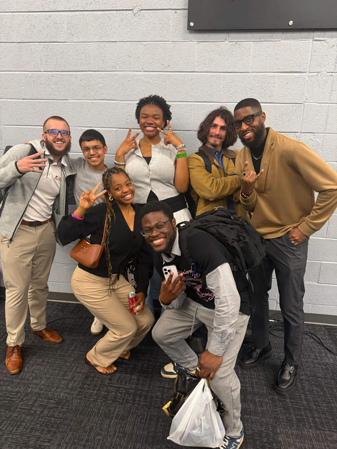 Seven students posed together against a painted wall, several making peace signs.