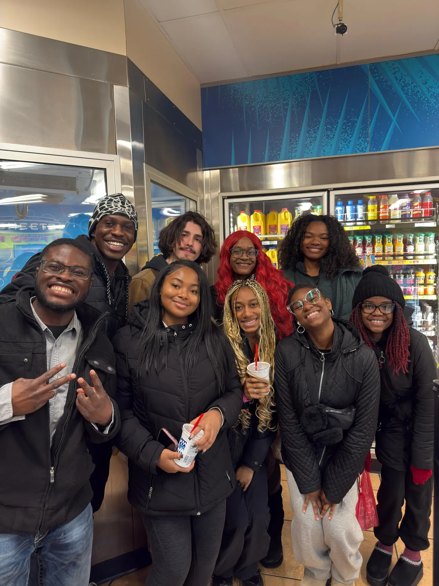 A group of students crowded together inside a shop at night, several of them holding drinks.