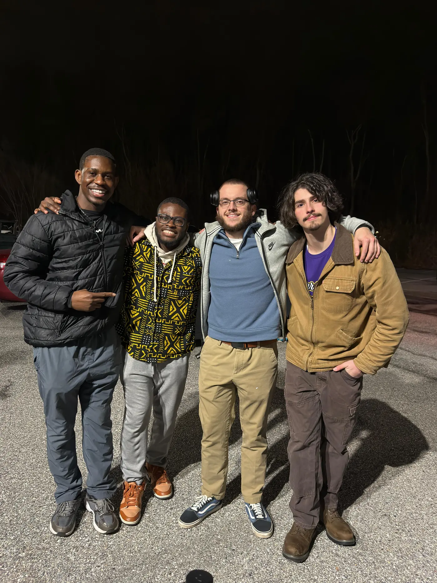 Four students standing together outside at night with their arms around each other.