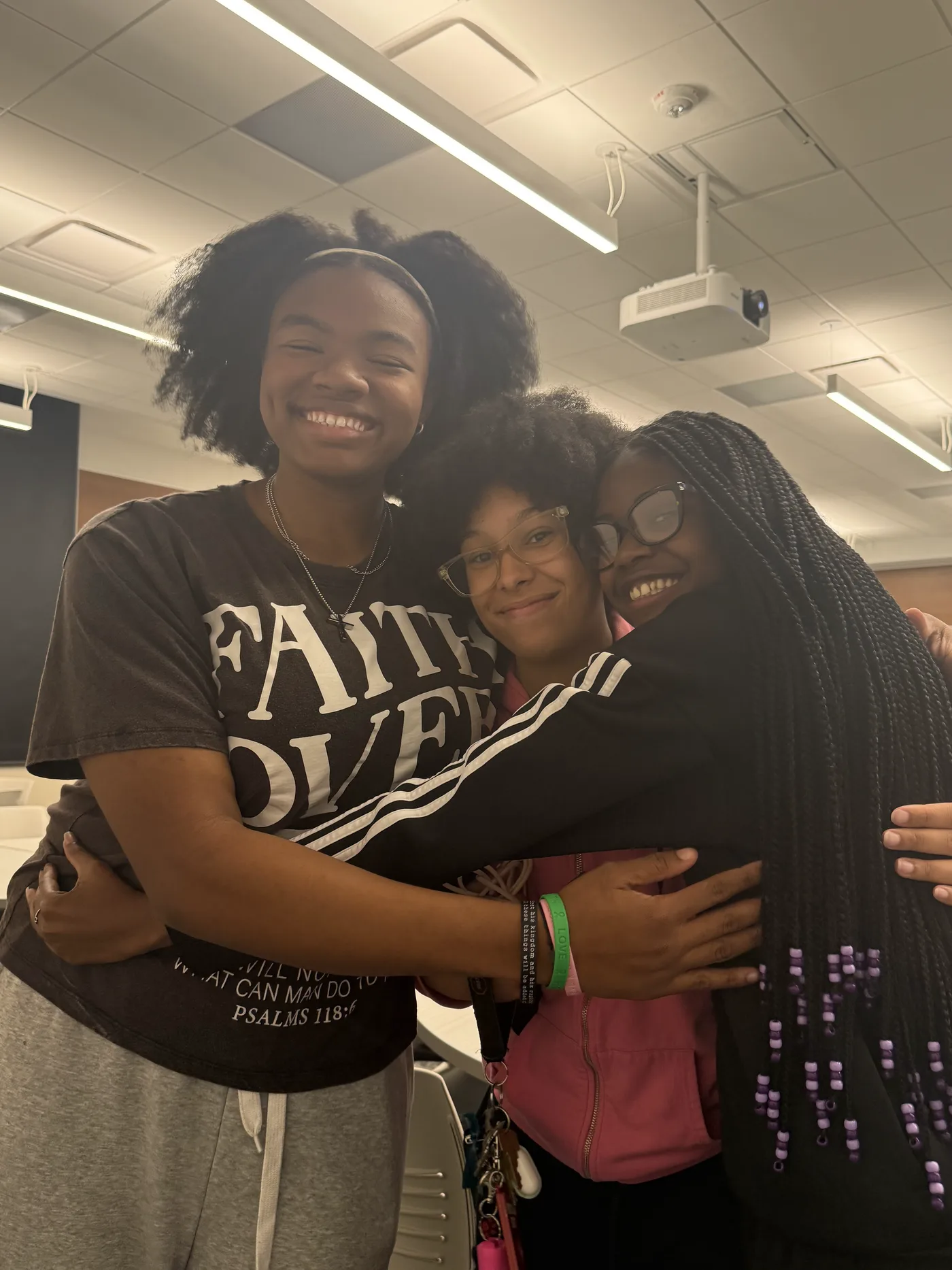 Three students holding on to each other and laughing in a classroom.