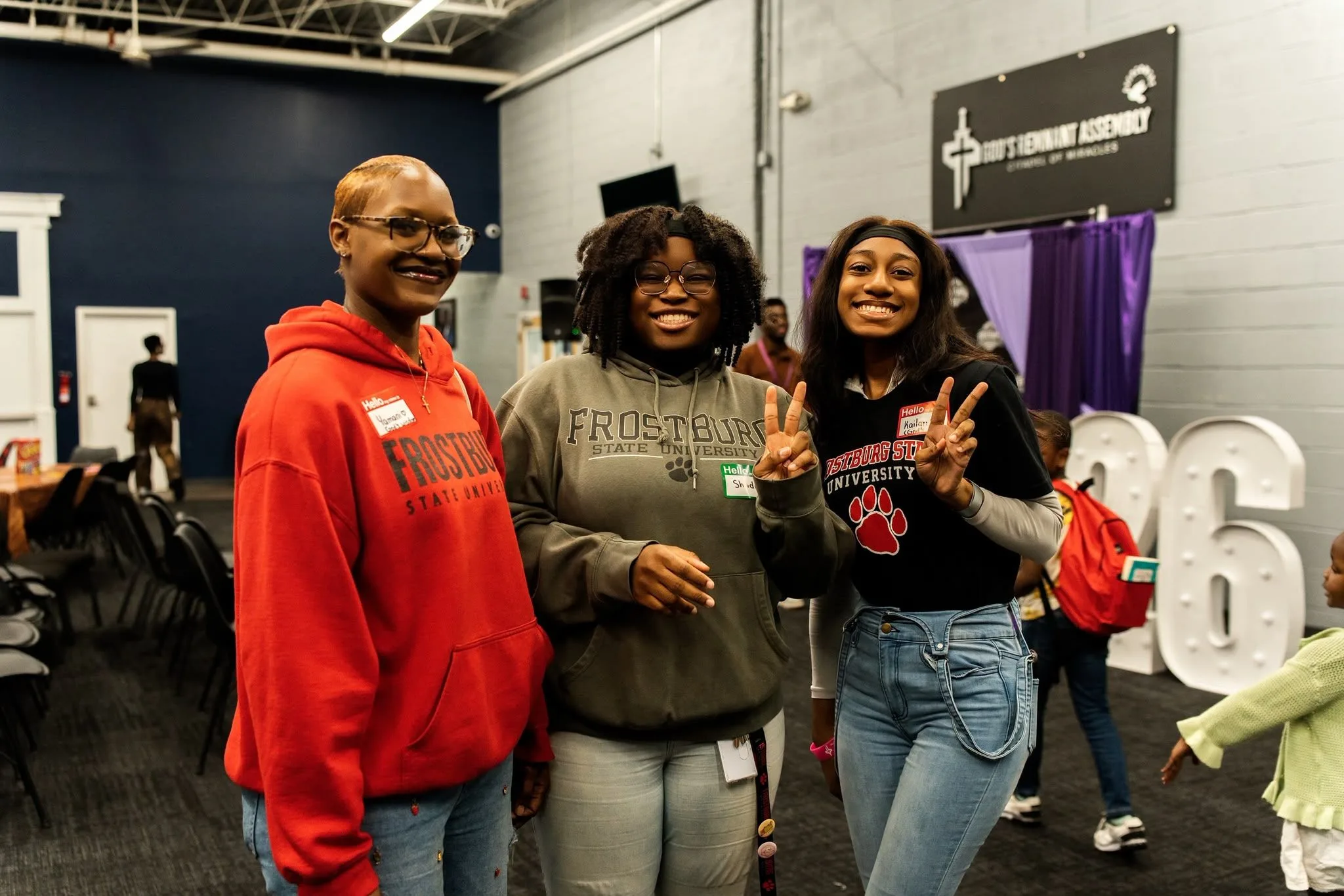 Three students standing together at an event in Frostburg State sweatshirts, two of them making peace signs.