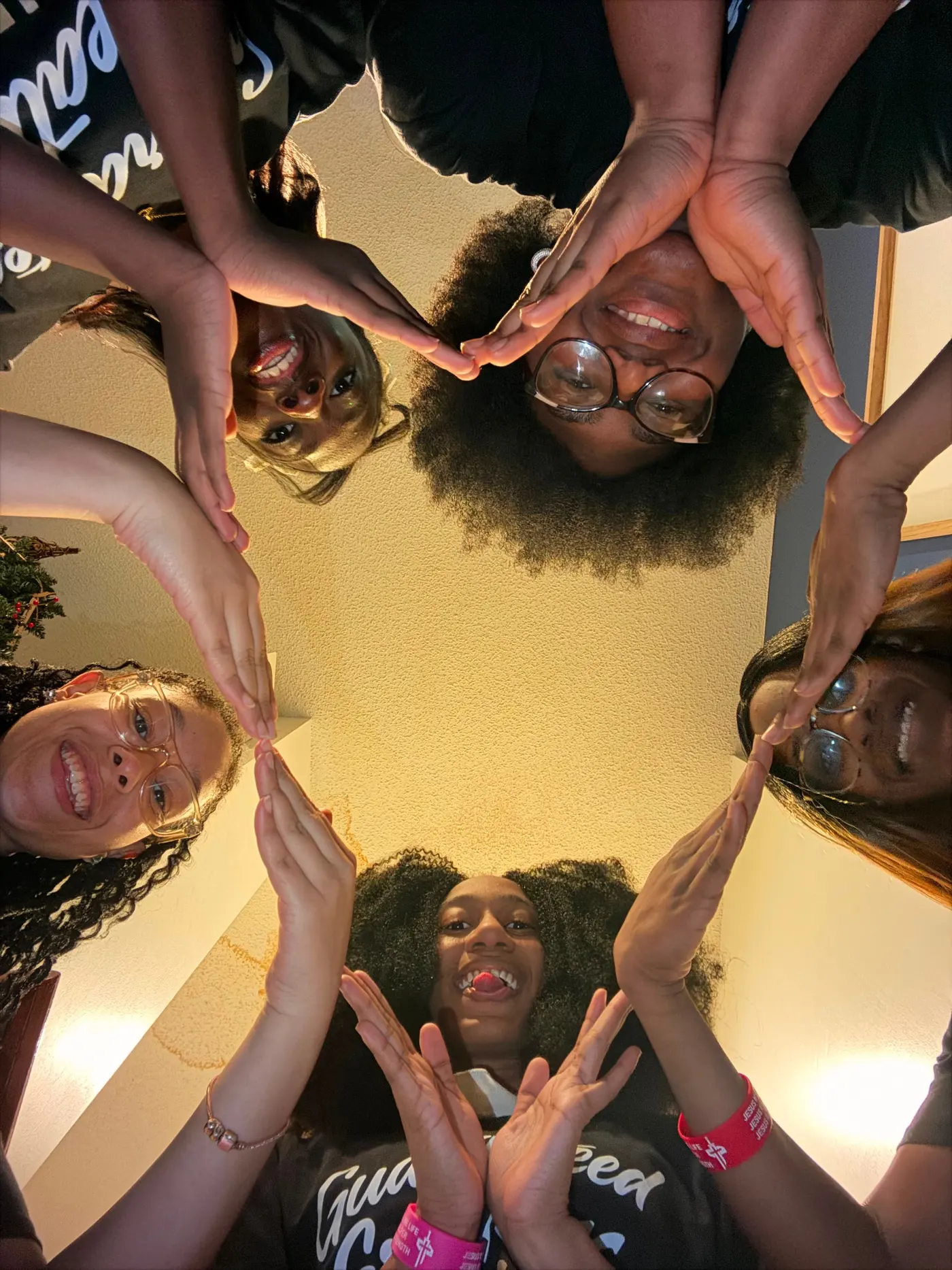 Five students photographed from below, leaning into a ring with their hands meeting above the camera.