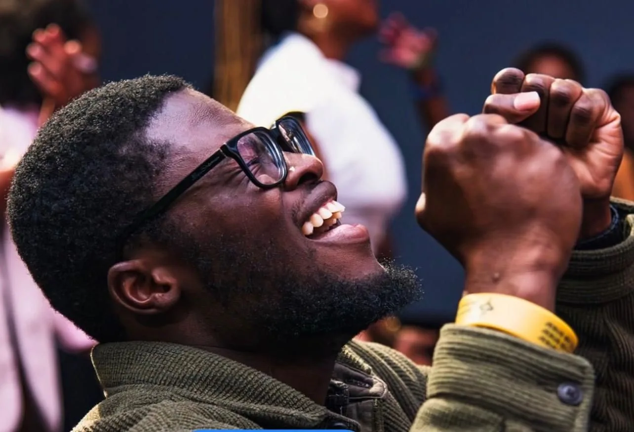 A student laughing with their eyes closed and one fist raised, others standing behind them out of focus.