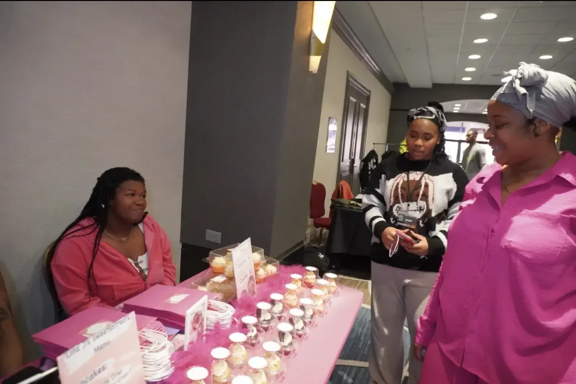 Students talking across a table laid with cupcakes and baked goods at a campus bake sale.