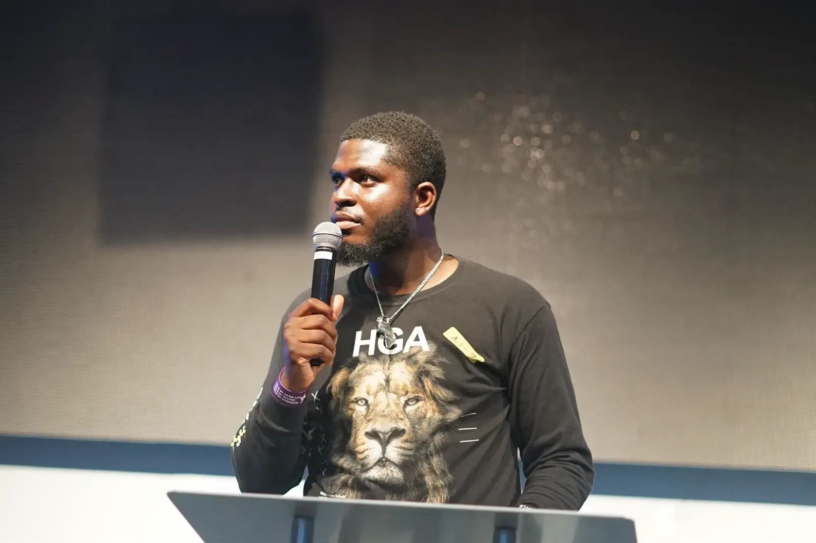 A speaker at a lectern holding a microphone, looking out at the room.